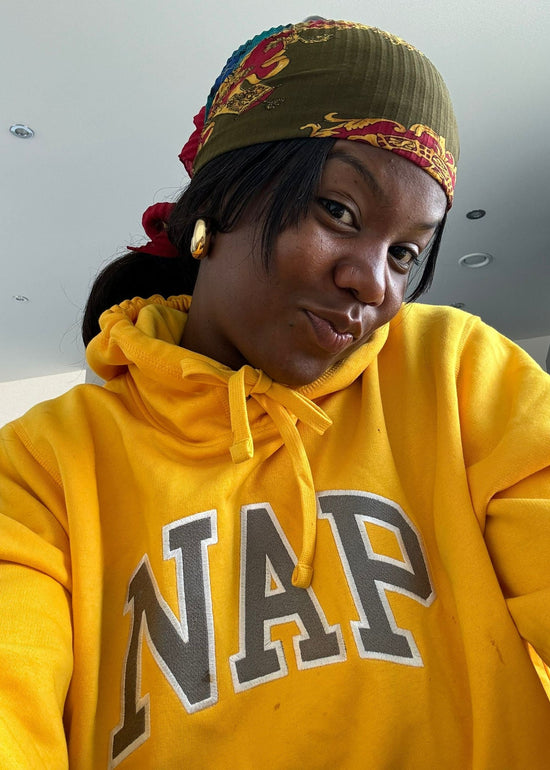 Person wearing a yellow hoodie with 'NAP' text and a colorful headband indoors.